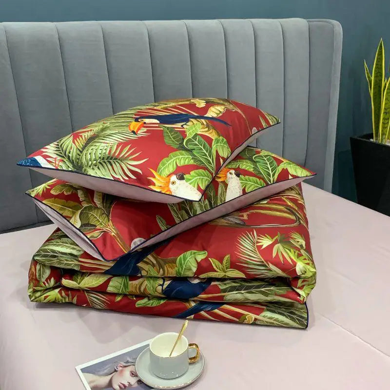 Two pillows resting on a folded duvet from the Elysian Garden Bedding Set, featuring a vibrant print of exotic birds and leaves, adding a touch of luxury and elegance to your bedroom decor.