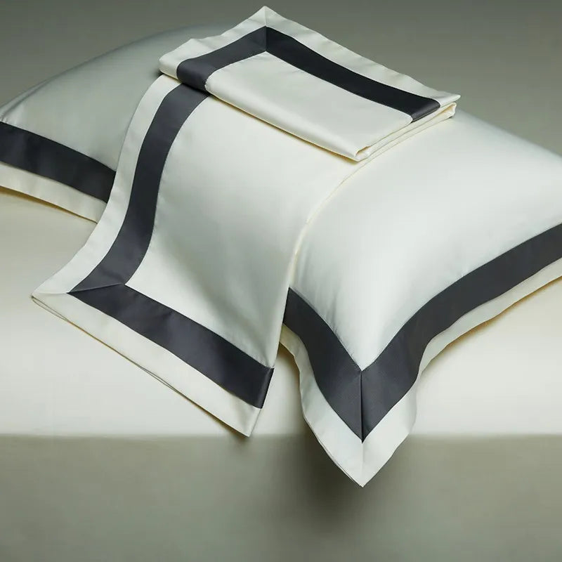 Close-up of Cleo Egyptian Cotton Pillowcase in white with dark gray borders, draped over a pillow, highlighting the softness and smooth texture of the fabric for luxurious comfort and style.