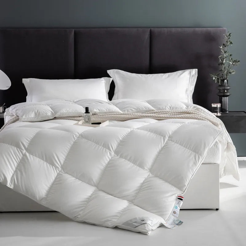 Seraph comforter in white, displayed on the bed. Crafted from 100% cotton with an 80 fabric count, this comforter offers a soft, breathable feel and lasting durability. Filled with premium white goose down for warmth and a fluffy, cloud-like texture, it’s perfect for all seasons. The elegant solid color design enhances any bedroom, and it's available in Queen and King sizes.