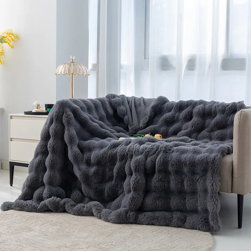 Cocoonette Rabbit Plush Blanket in dark gray draped over a sofa, offering luxurious warmth and comfort to enhance the style and coziness of any room.