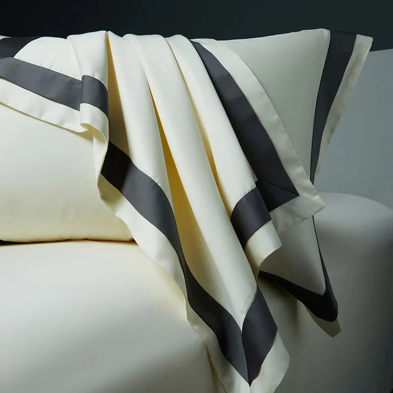 Close-up of Cleo Egyptian Cotton Flat Bedsheet in white with dark gray borders, draped over the pillowcase, showcasing the luxurious softness and smooth texture of the fabric. This 4-piece set offers ultimate comfort and style for your bedroom.