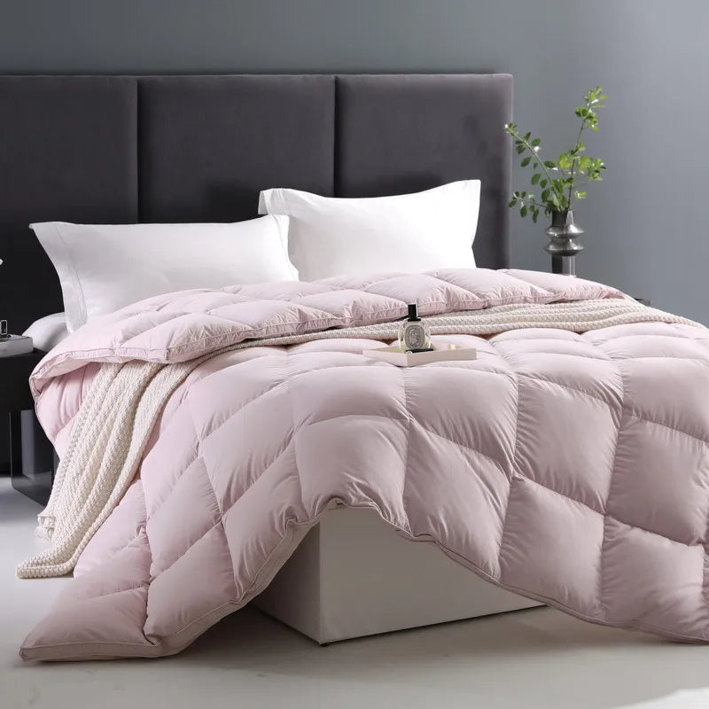 A beautifully arranged bed with a 100% cotton comforter in soft light pink, filled with premium white goose down for a fluffy, breathable feel. The solid color design enhances the look of the neatly placed pillows, creating a warm and inviting atmosphere. Available in Queen and King sizes.