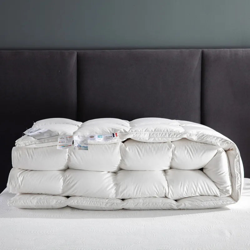 A beautifully folded Seraph comforter in white, made from 100% cotton with an 80 fabric count. The comforter features premium white goose down fill, providing a soft, breathable texture and a fluffy, cloud-like feel. Its simple, elegant design emphasizes both comfort and durability, perfect for enhancing any bedroom. Available in Queen and King sizes.